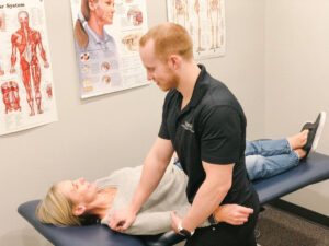 A Physiotherapist performing manual therapy on a client's shoulder as they lay on a client massage table.